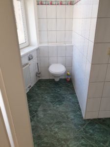 Toilette im Bad, grüne Fußbodenfliesen und weiße Wandfliesen. Bad mit Fenster
