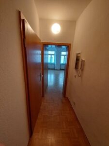 Flur mit braunem Parkettboden, weißen Wänden, Holztüren, Gegensprechanlage