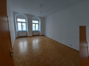 Zimmer mit braunem Parkettboden, weißen Wänden, zwei Fenstern, zwei Heizkörpern