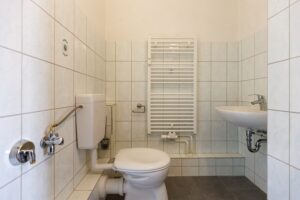 dunkle Fußbodenfliesen, weiße Wandfliesen, WC mit Spülkasten, Handtuchheizkörper weiß, weißes Waschbecken