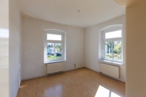 weiße Wände, weiße Decke, zwei weiße Fenster, weiße Heizkörper unter Fenster, brauner Parkettboden