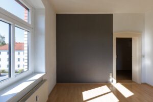 graue Wand, weiße Wand, beigefarbene Tür, weißes Fenster, brauner Parkettfußboden