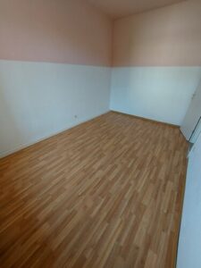 Zimmer mit braunem Parkettboden und farbig gestrichenen Wänden.