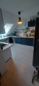 Küche mit Dachschräge und schwarzen Schränken, weißen Wänden und holzfarbenen Fußboden