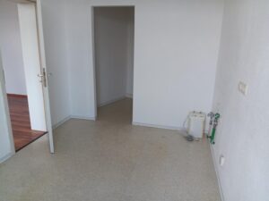 Küche mit grauem PVC-Belag und Anschlüssen an der rechten Wand, Wände weiß, Abstellnische, Tür ins Wohnzimmer