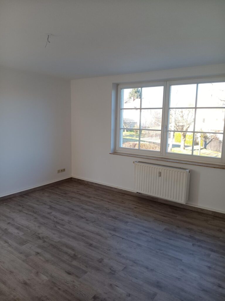 weiße Wände, weißes Doppelfenster, weißer Heizkörper unter Fenster, brauner Parkettfußboden