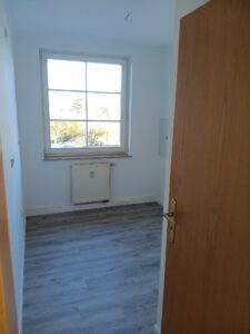 brauner Parkettfußboden, weiße Wände, Fenster mit weißem Fensterrahmen, weißer Heizkörper unter Fenster