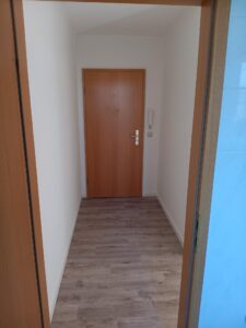 brauner Parkettfußboden, weiße Wände, braune Holzeingangstür