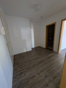 Zu sehen ist ein Flur mit weißen Wänden, holzfarbenen Zimmertüren und holzfarbenen Boden