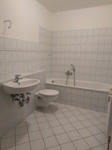Zu sehen ist ein Bad mit weißen Fliesen, Waschbecken, Badewanne und Toilette