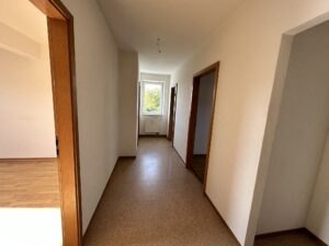 Blick in den Flur mit PVC-Boden und Fenster am Ende des Ganges, kleiner Nische und den Türen zu den Zimmern