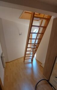 Zimmer mit Treppe, brauner Laminatfußboden, weiße Wände, Fenster