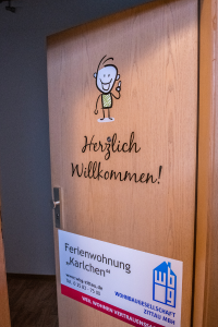 offen stehende Wohnungseingangstür , wo ein das Logo der WBG Zittau zu sehen ist und mit folgendem Schriftzug versehen ist: Herzlich Willkommen - Ferienwohnung "Karlchen", Telefon: 03583-7500