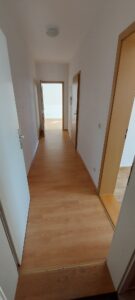 hellbrauner Laminatboden, weiße Wände, drei braune Holzzimmertüren, Lampe an Decke, weiße Eingangstür