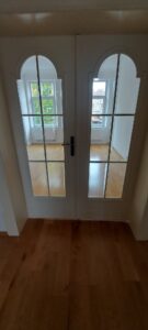 brauner Parkettboden, weiße Holztür mit Glasausschnitten, dahinterliegender Raum