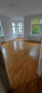 brauner Parkettboden, weiße Wände, fünf weiße Fenster, Stuckverzierungen an Decke