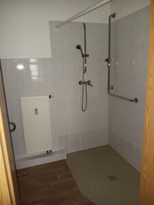 weiße Wandfliesen, braune Bodenfliesen, ebenerdige Dusche, silberne Armaturen, weißer Heizkörper