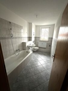 graue Fußboden- und Wandfliesen, Bad mit weißer Badewanne, weißes Fenster