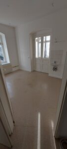 weiße Wände, weiße Tür in Wintergarten, weißer Waschbecken, brauner Linoleumbelag