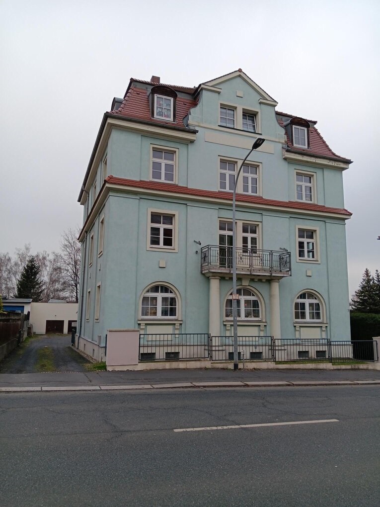 4 stöckiges Haus mit hellgrüner Fassade, rotem Dach und davor eine Straße