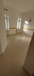 weiße Wände, zwei weiße Fenster, brauner Linoleumbelag