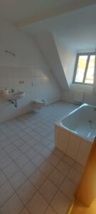 weiße Fußbodenfliesen, weiße Wandfliesen, Dachschräge, grünes Holzrahmenfenster, weißer Waschbecken mit Mischbatterie, weiße Badewanne, braune Zimmertür