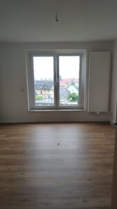 Raum mit holzfarbenen Fußboden und weißen Wänden. Vorne ein Fender und ein weißer Heizkörper