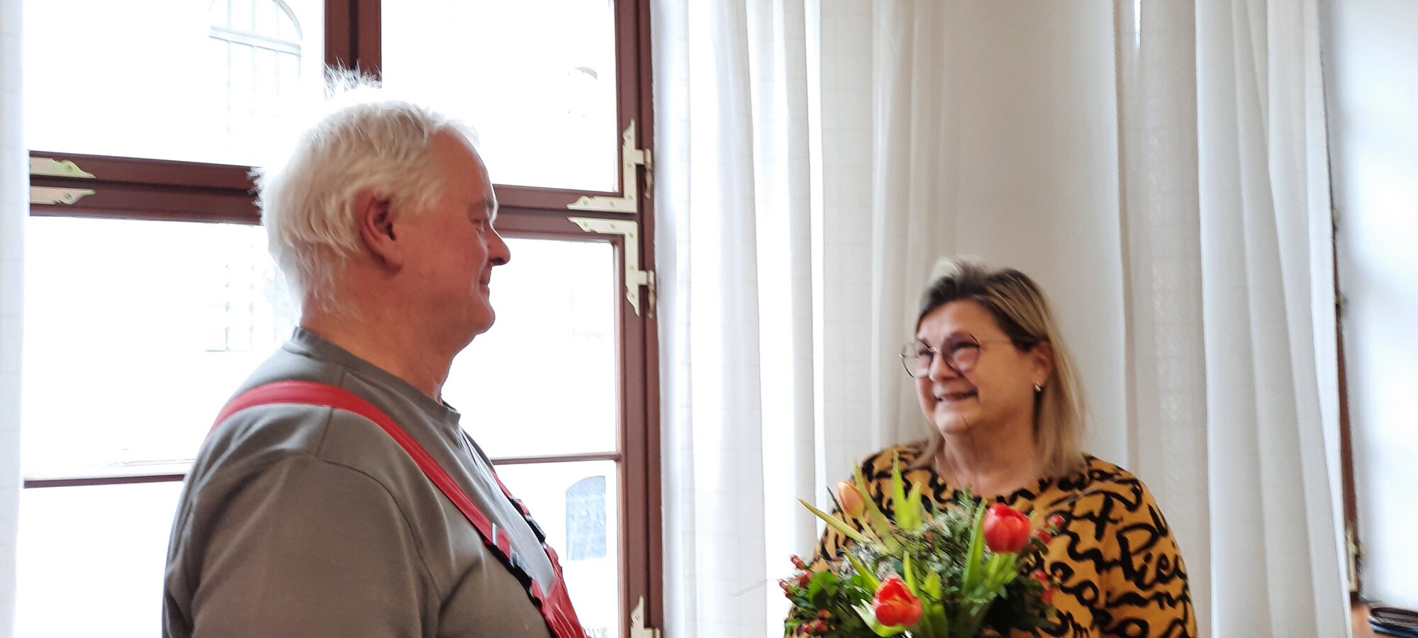 Zusehen ist Frau Standke und Herr Püschel von der WBG Zittau. Frau Standke übergibt Herrn Püschel einen Blumenstrauß