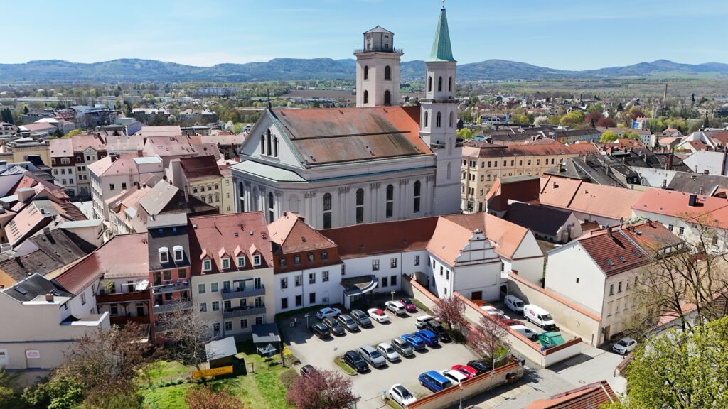 Zu sehen ist auf dem Luftbild das Gebäude der WBG Zittau von oben. Dahinter sieht man die Johanniskirche, die Stadt Zittau und das Zittauer Gebirge.
