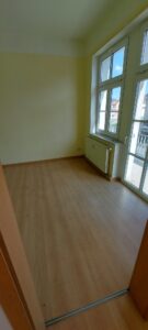 brauner Laminatfußbodenbelag, braune Holztür, gelb gestrichene Wände, weißes Kunststofffenster und weiße Balkontür