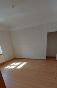 brauner Laminatfußbodenbelag, braune Holztür, mintgrün gestrichene Wände, weißes Kunststofffenster
